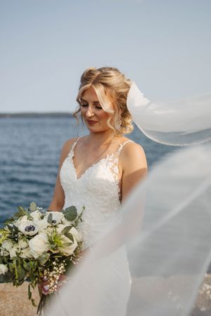 A flowing white wedding dress and bouquet photographed at a scenic beach setting.