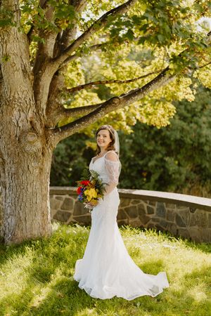 A bride in a flowing white gown twirls gracefully under a large tree in golden afternoon sunlight.