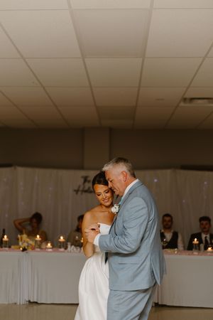 A tender dance scene unfolds at a wedding reception as two figures share a moment under white ceiling lights.