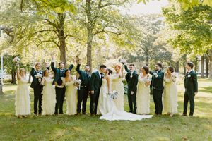 Wedding party in navy and cream attire poses outdoors in elegant formation under sunlit autumn trees.
