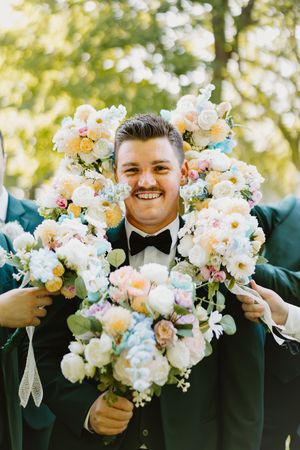Joyful moment captured at wedding with emerald green suits and lush floral arrangements in peach and white tones.