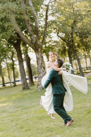 A couple dancing and spinning in a romantic outdoor setting among trees on a grassy slope, creating a joyful moment.