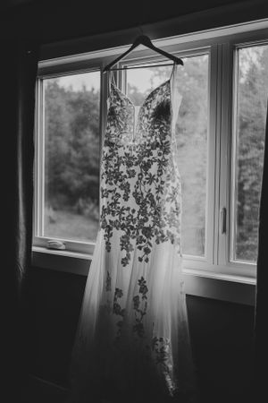 Wedding dress hangs in window with natural light streaming through.
