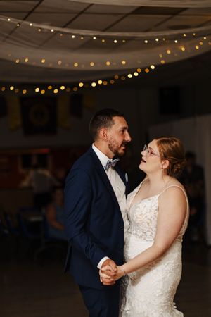 Newlyweds dancing intimately under string lights at indoor reception venue.