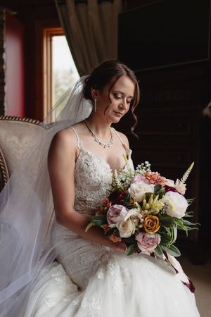 An elegant lace wedding dress with a beautiful mixed floral bouquet in soft lighting.