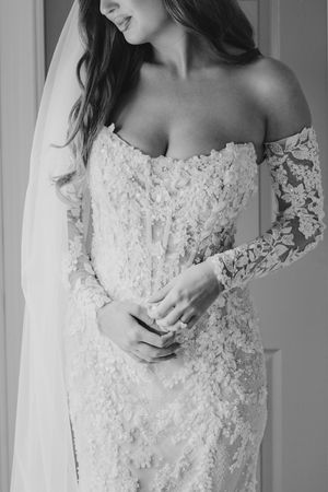 Black and white photo of a bride in an off-shoulder lace wedding gown with long sleeves and veil.