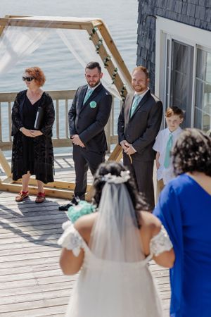 Wedding ceremony on waterfront deck with guests watching couple exchange vows.