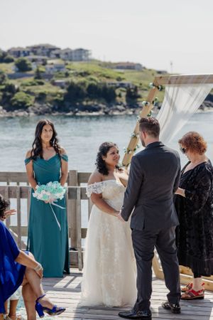 Wedding party helps fluff out a white wedding dress on an oceanside deck.