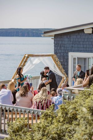 Wedding guests gather on a waterfront deck with shingle siding and coastal views.