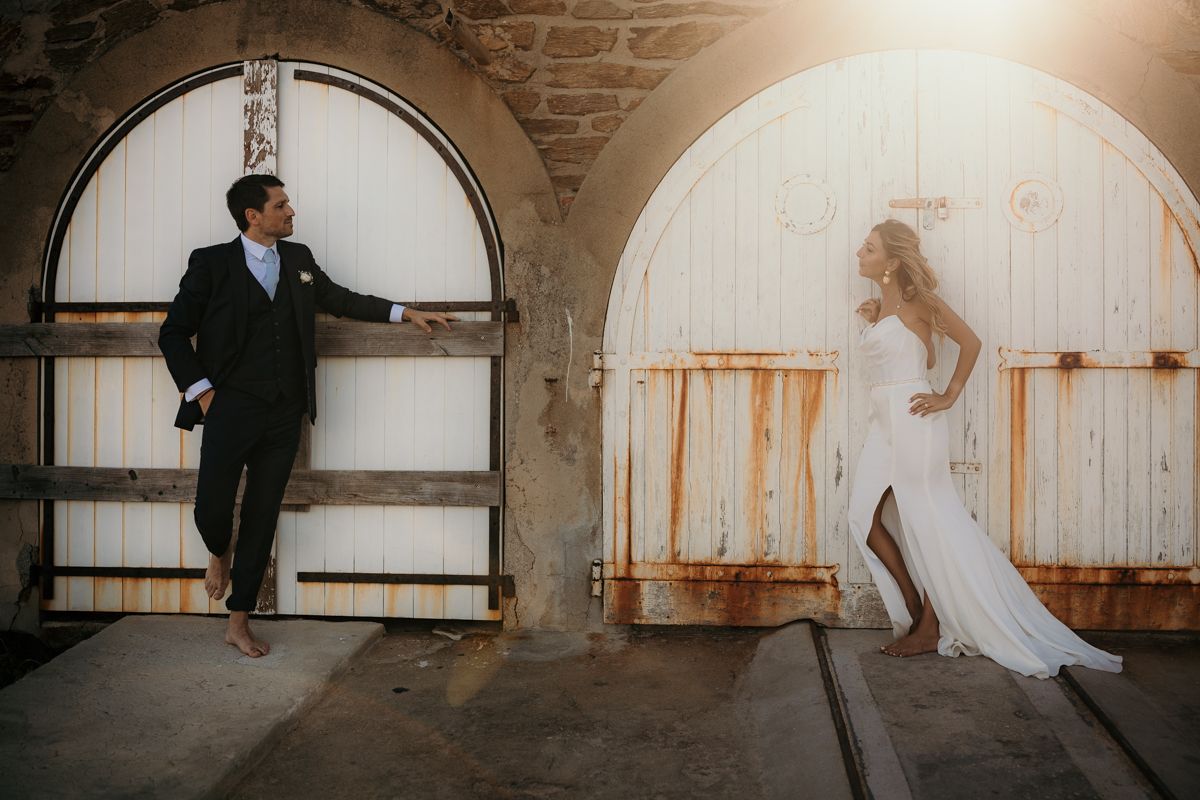 Wedding couple poses playfully in stone archways with dramatic lighting.
