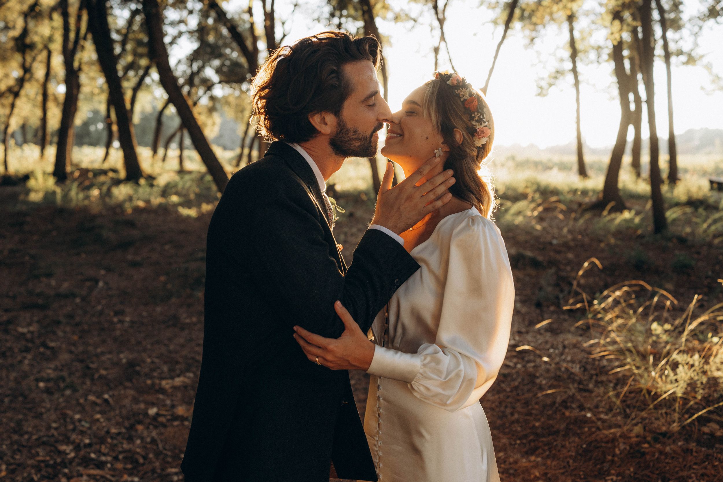 A couple shares a romantic moment together in a wooded setting during golden hour.