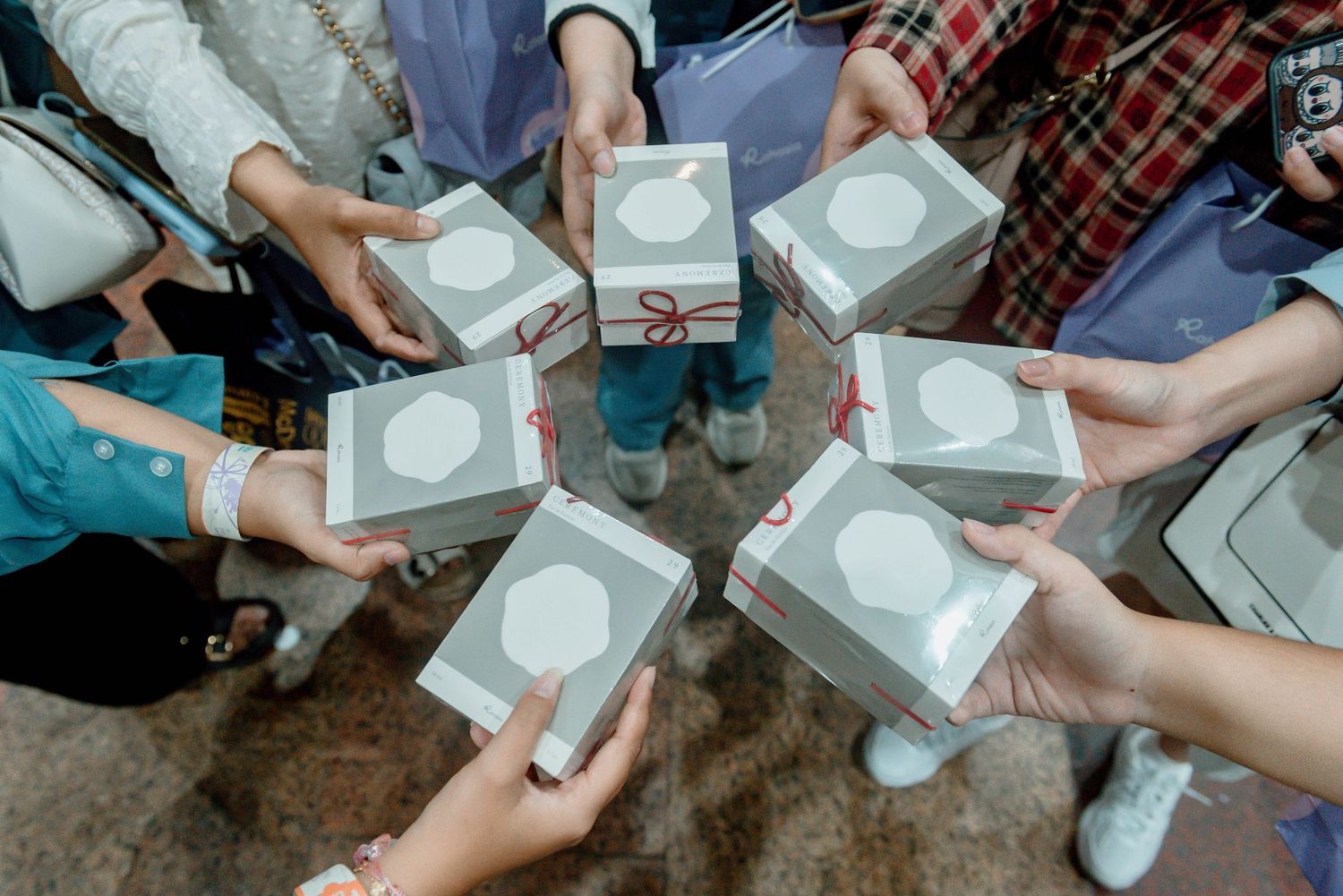 Multiple hands hold up identical white product boxes in a circular formation showing off new tech purchases.