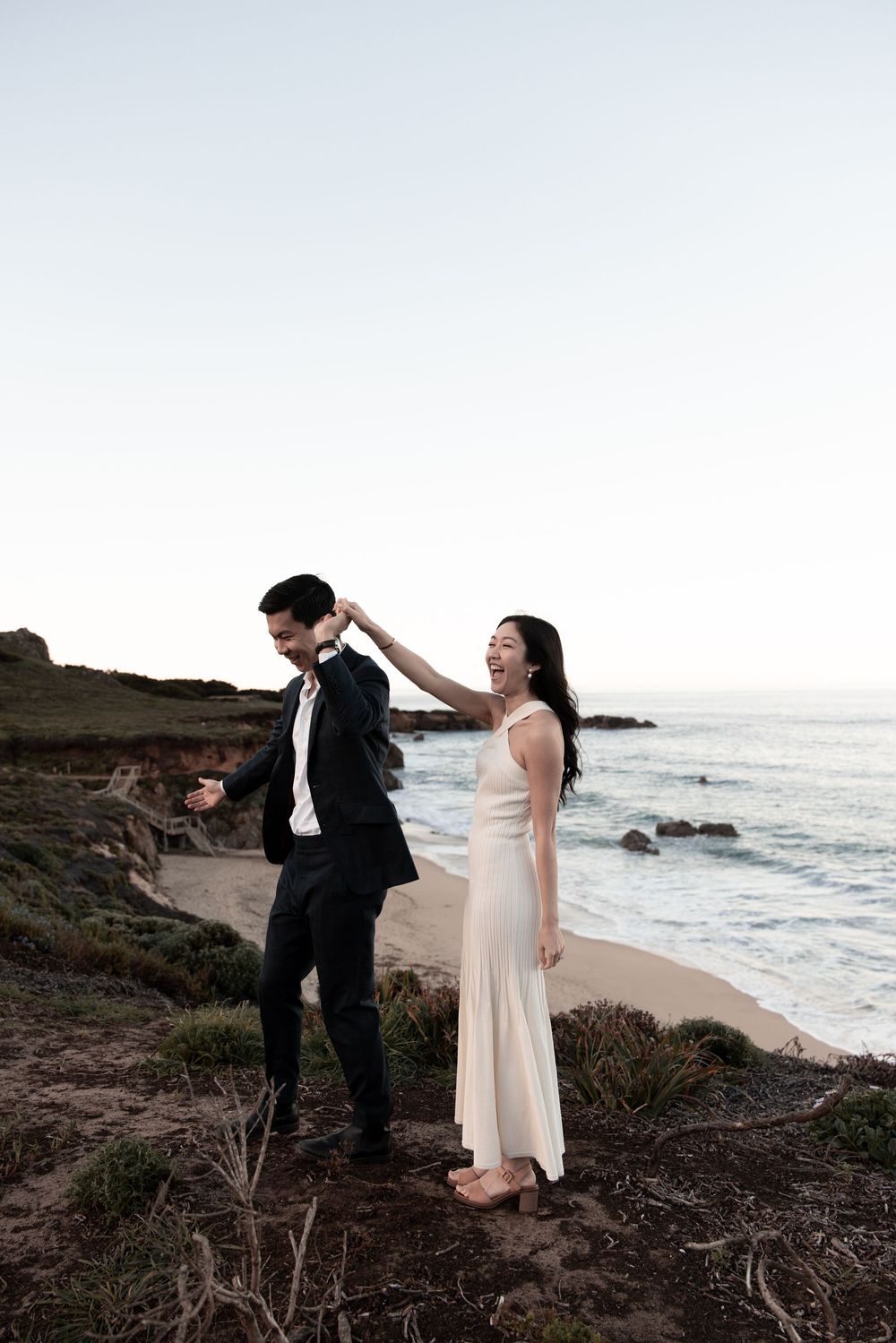 A couple shares romantic moments on a scenic coastal cliff overlooking the ocean at sunset.
