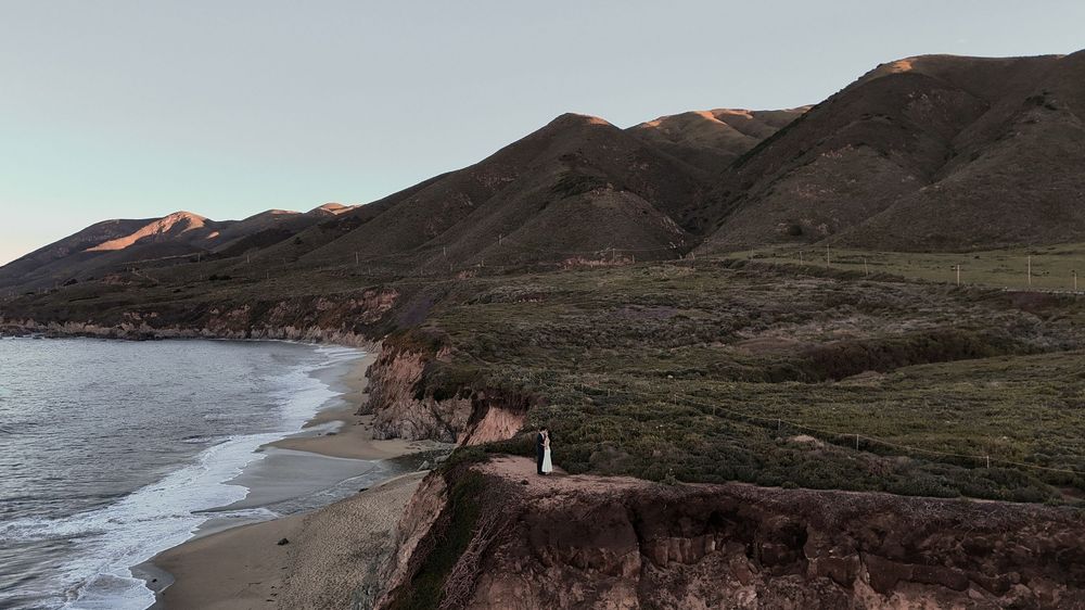 Winding coastal road along rugged cliffs and sandy beach at Big Sur during golden hour.