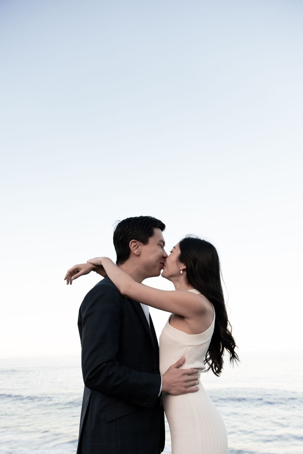 A romantic couple embraces on the beach in a series of intimate poses against an ocean backdrop.