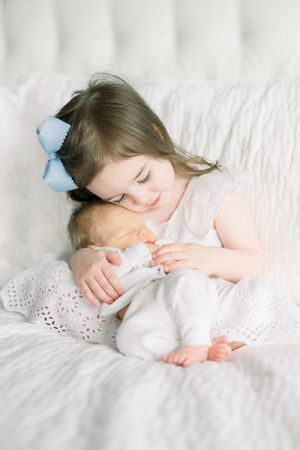 a big sister holds her newborn sister at a newborn session in washington dc