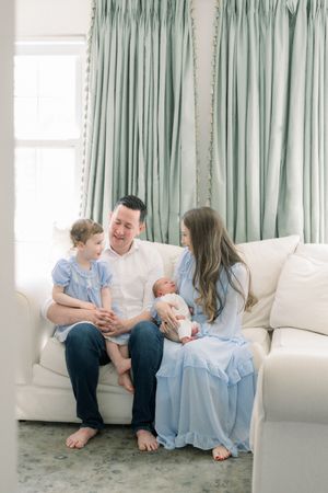 A family wearing light blue and white sits together on a white couch at a newborn photography session in washington dc