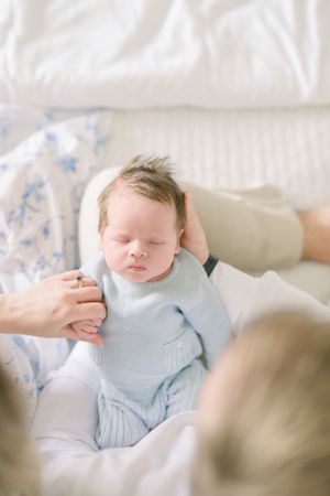 A sleeping newborn baby wearing light blue clothing rests peacefully on white bedding taken by a dc newborn photographer