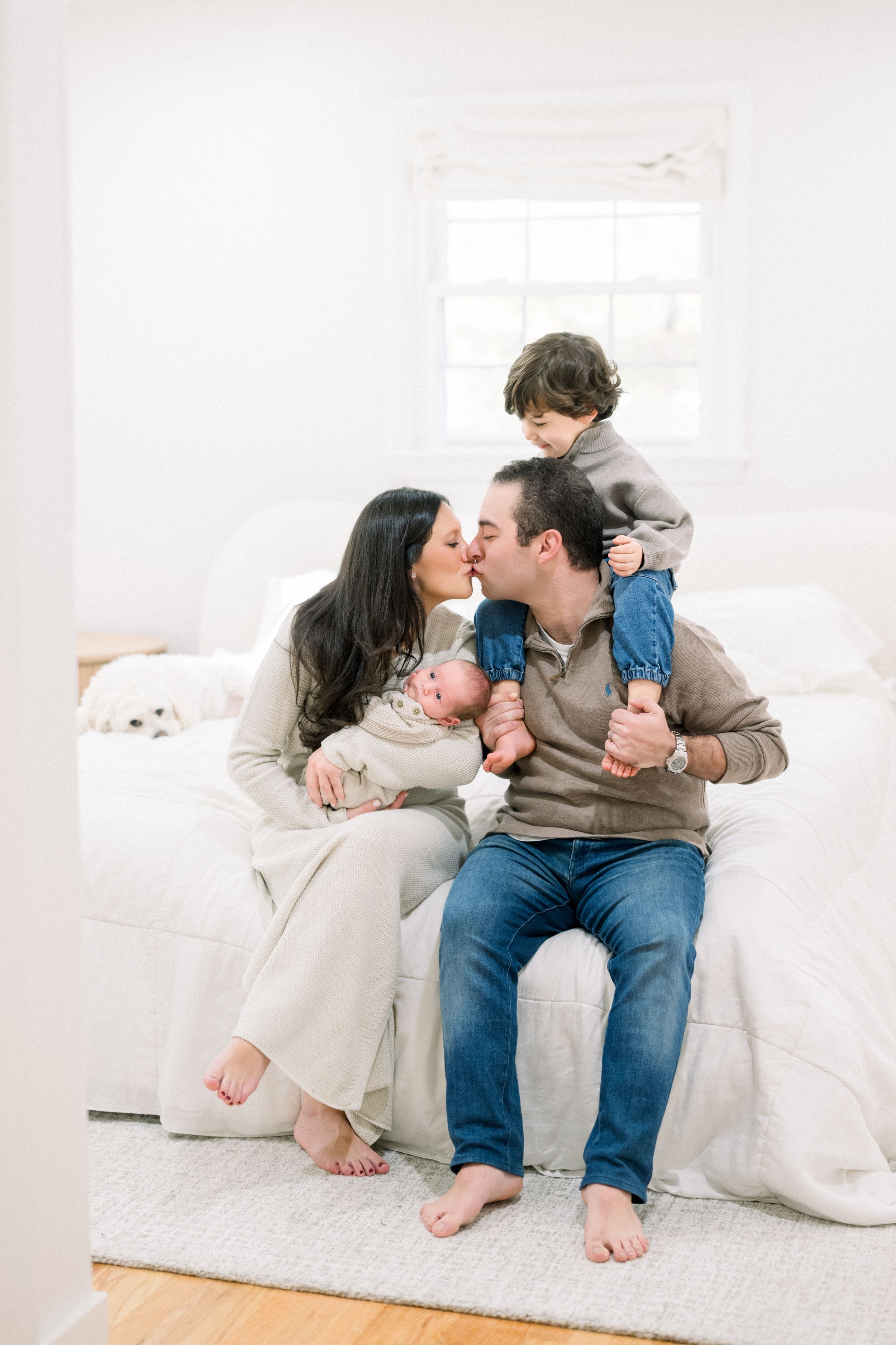 a family smiling together on a bed holding their newborn at a newborn session in washington dc