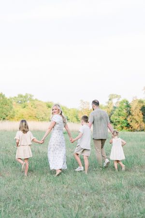 A family holding hands while walking through a grassy meadow on a sunny summer day in northern virginia