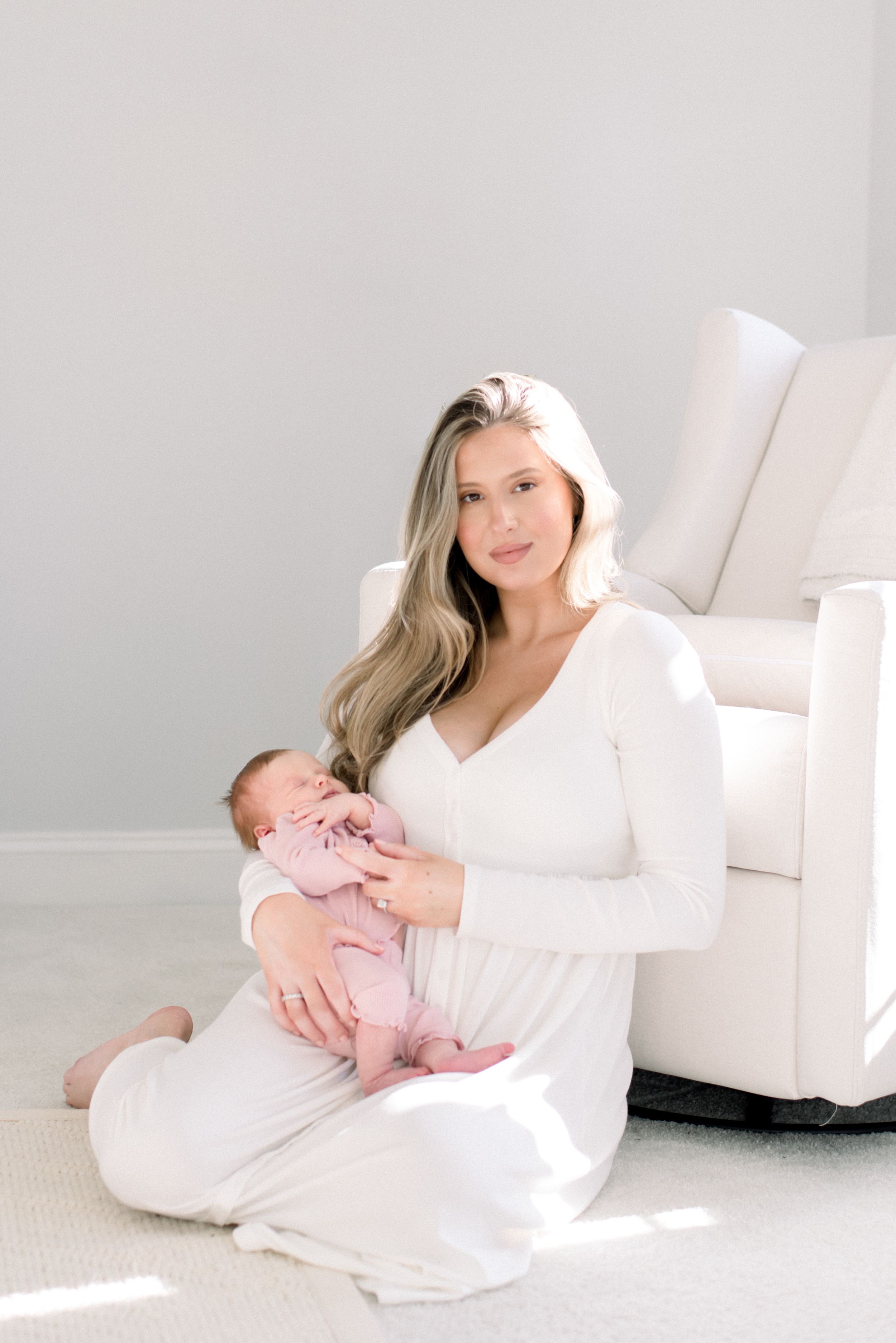 Mother in white dress sits with baby an a natural light in-home photo session in washington dc