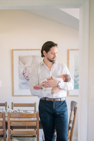 a dad stand under archway in his home holding his newborn at an in-home newborn session in northern virginia
