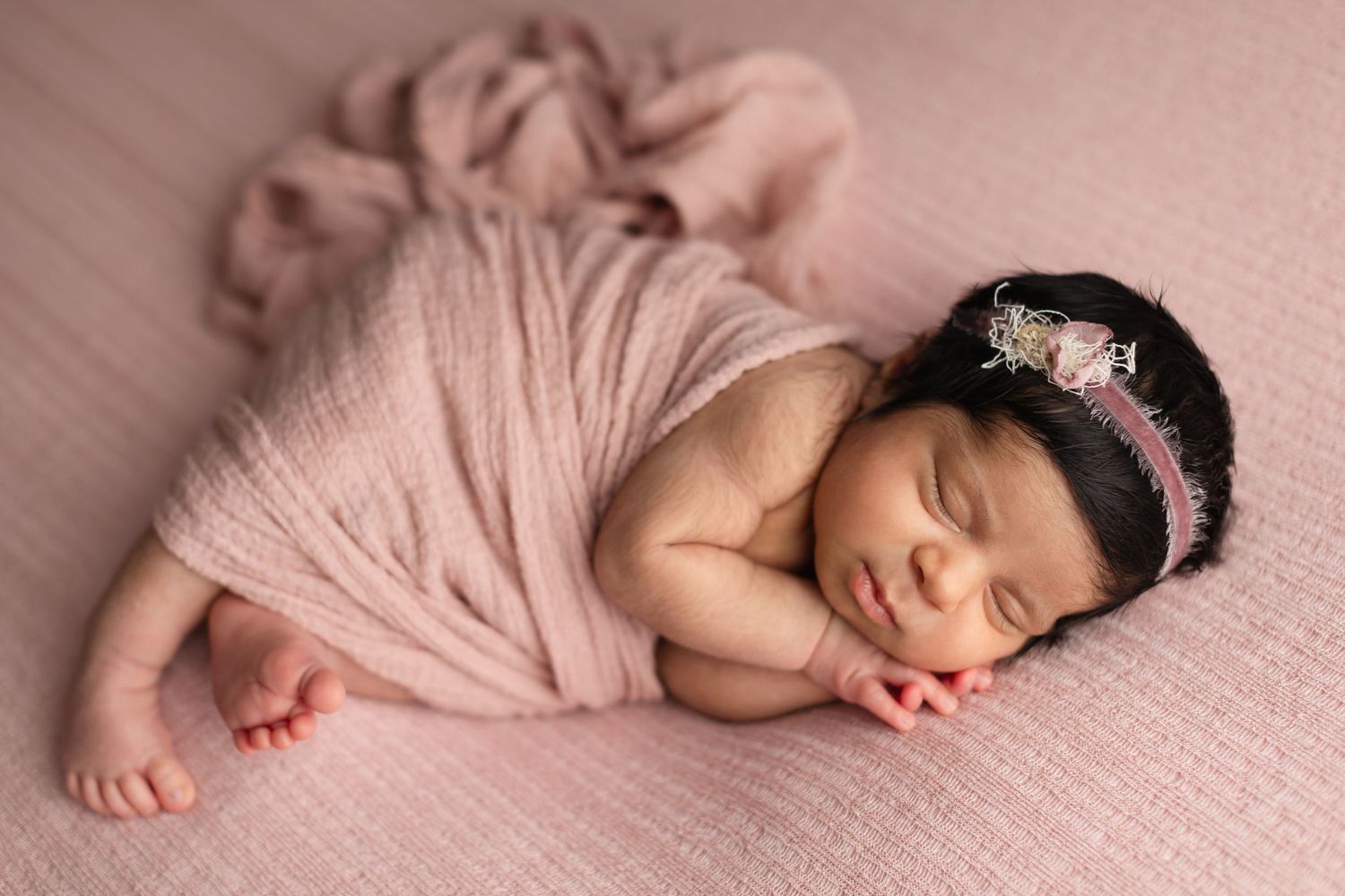 A sleeping newborn baby lies peacefully on soft pink fabric in a series of artistic close-up photographs. Elizabeth Lang Photography Surrey