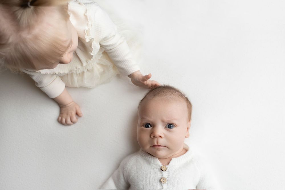 Big sister gently touching newborn baby, taken by Jen Knightstep, Photographer