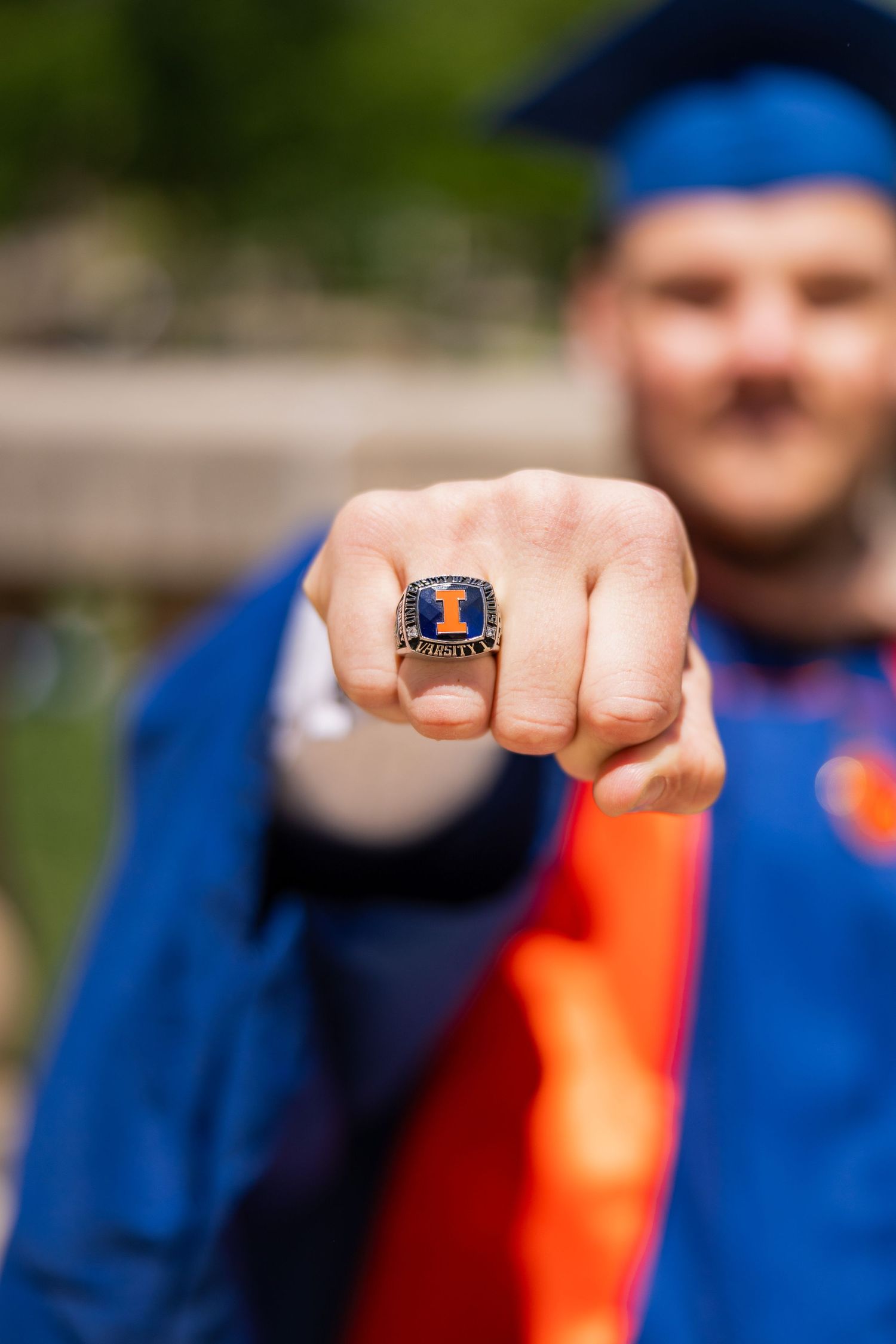 UIUC graduating student showing off a U of I ring while wearing a cap and gown at Foellinger