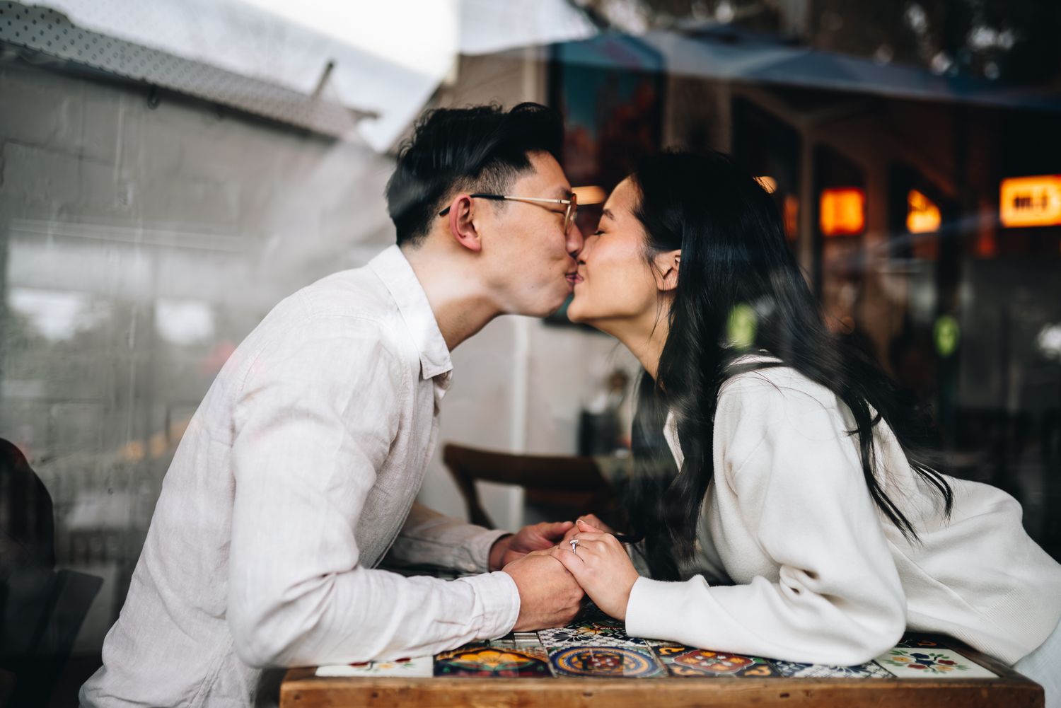A couple in white attire shares a romantic moment while seated together in a Melbourne cafe during a prewedding photo session.