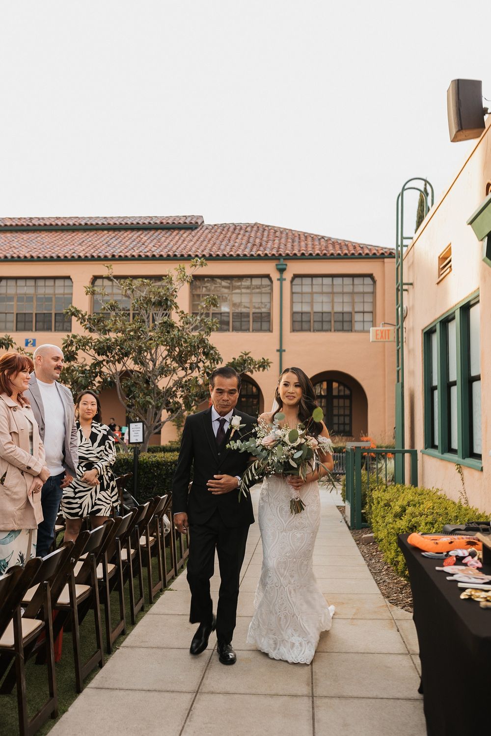 A bride and her dad walk down the aisle at an outdoor wedding ceremony at Stone Brewing Liberty Station in San Diego.