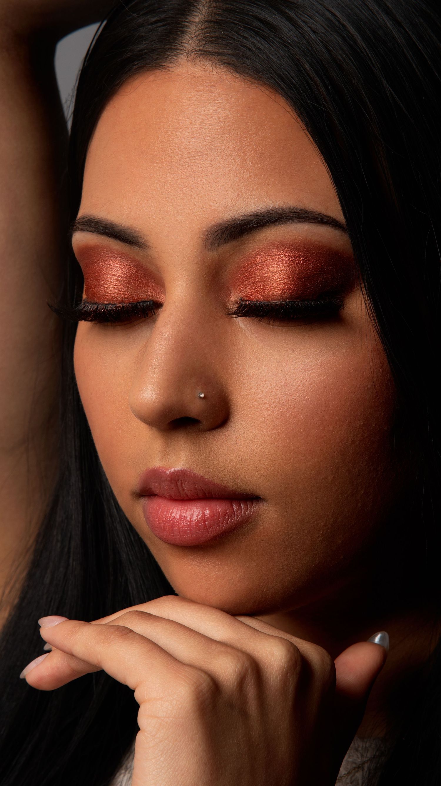 Close-up portrait of woman with striking red shimmer eyeshadow and nose ring, eyes closed.