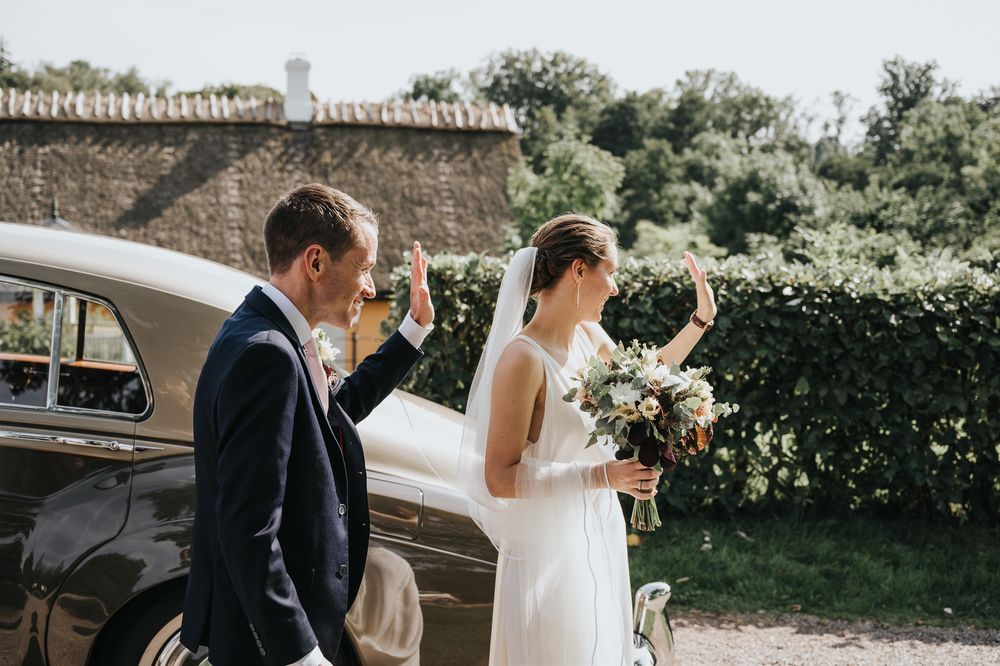 Wedding celebration scene outside with floral arrangements and vintage car.