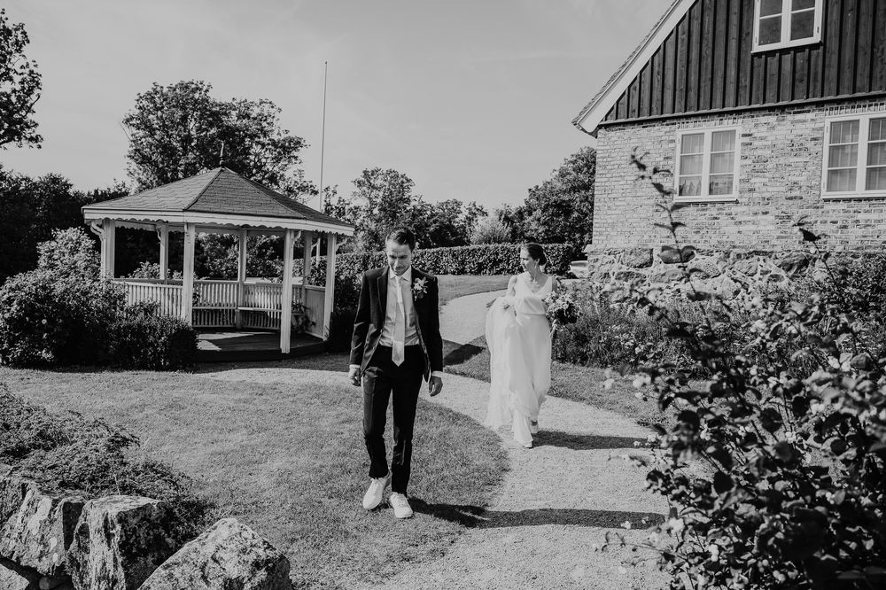Wedding party walking outside a rustic farmhouse with white siding and green landscaping.
