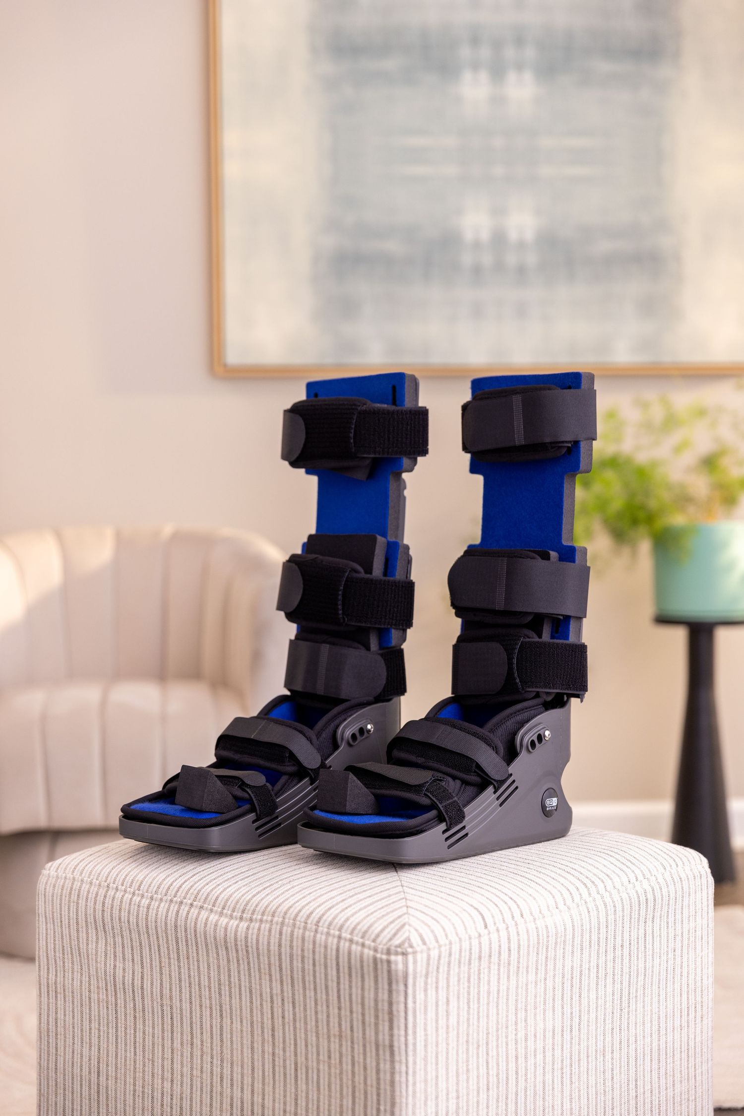 Pair of blue medical walking boots with adjustable straps on white furniture.