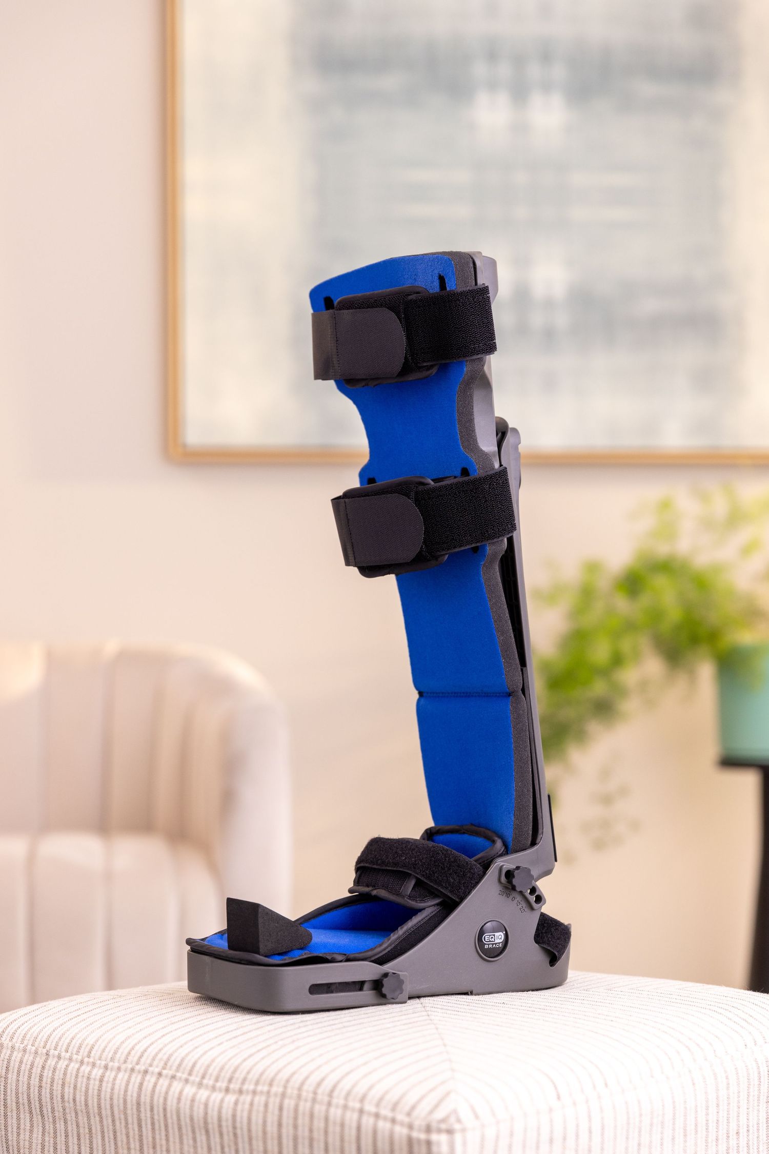 Blue medical walking boot with black straps displayed on light colored ottoman.
