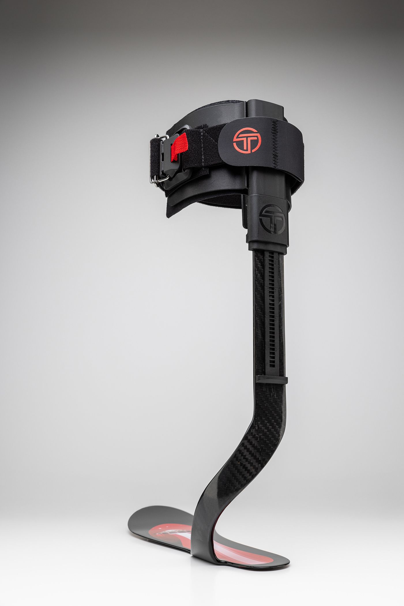 Black prosthetic leg with red accents and curved design against grey background.
