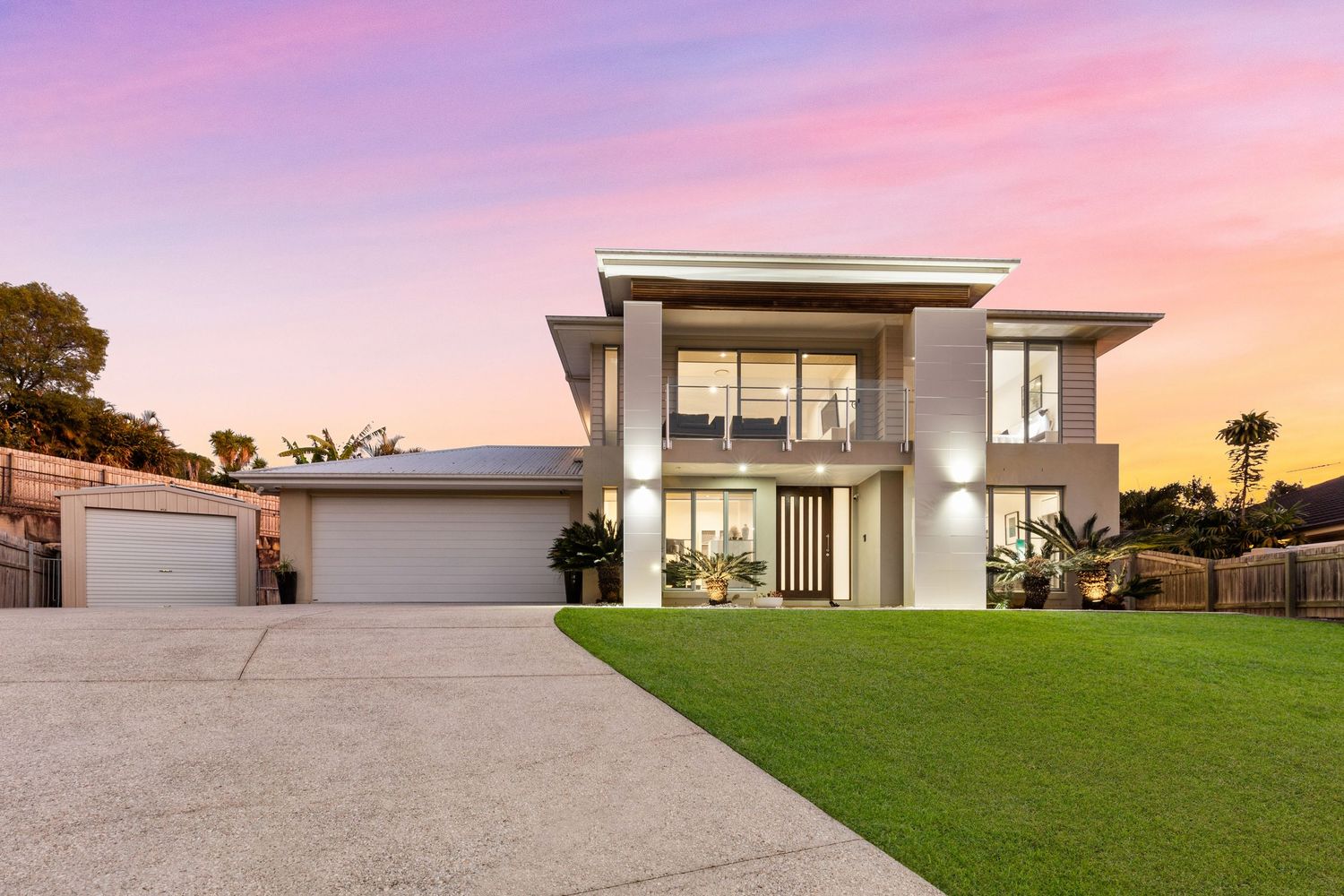 Modern two-story home with neutral facade, double garage, lush lawn, and stunning pink and purple sunset sky.