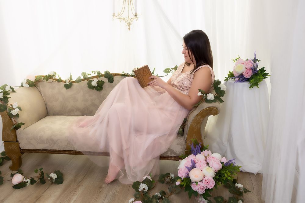 A woman in a pink dress sits on a floral couch surrounded by flowers.
