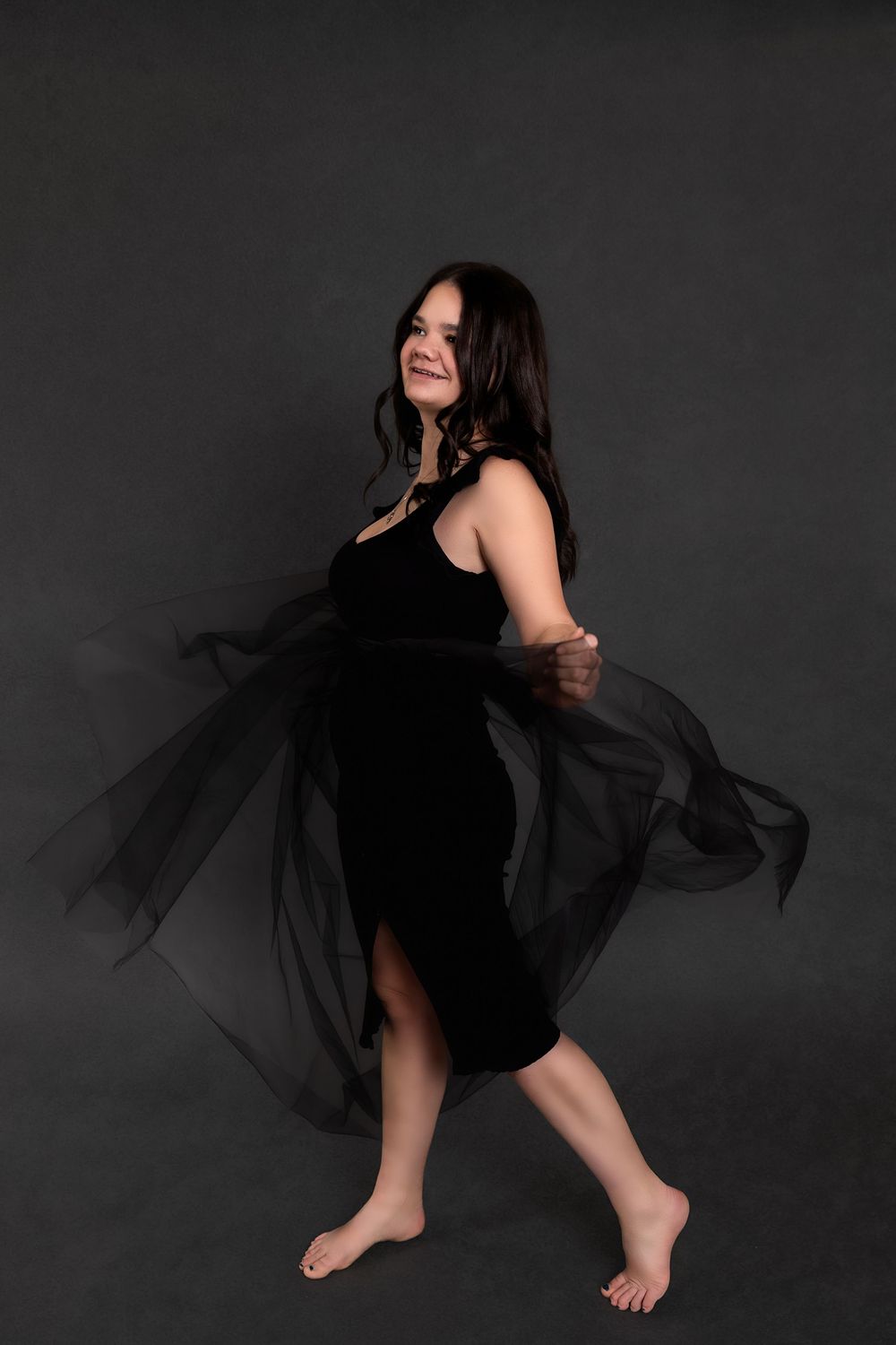A dancer in a flowing black dress performs an expressive movement sequence against a dark background.