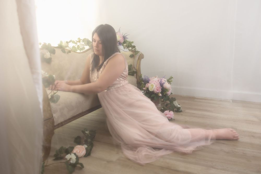 A woman in a pink dress sits on a floral-adorned bench in a serene, ethereal setting.