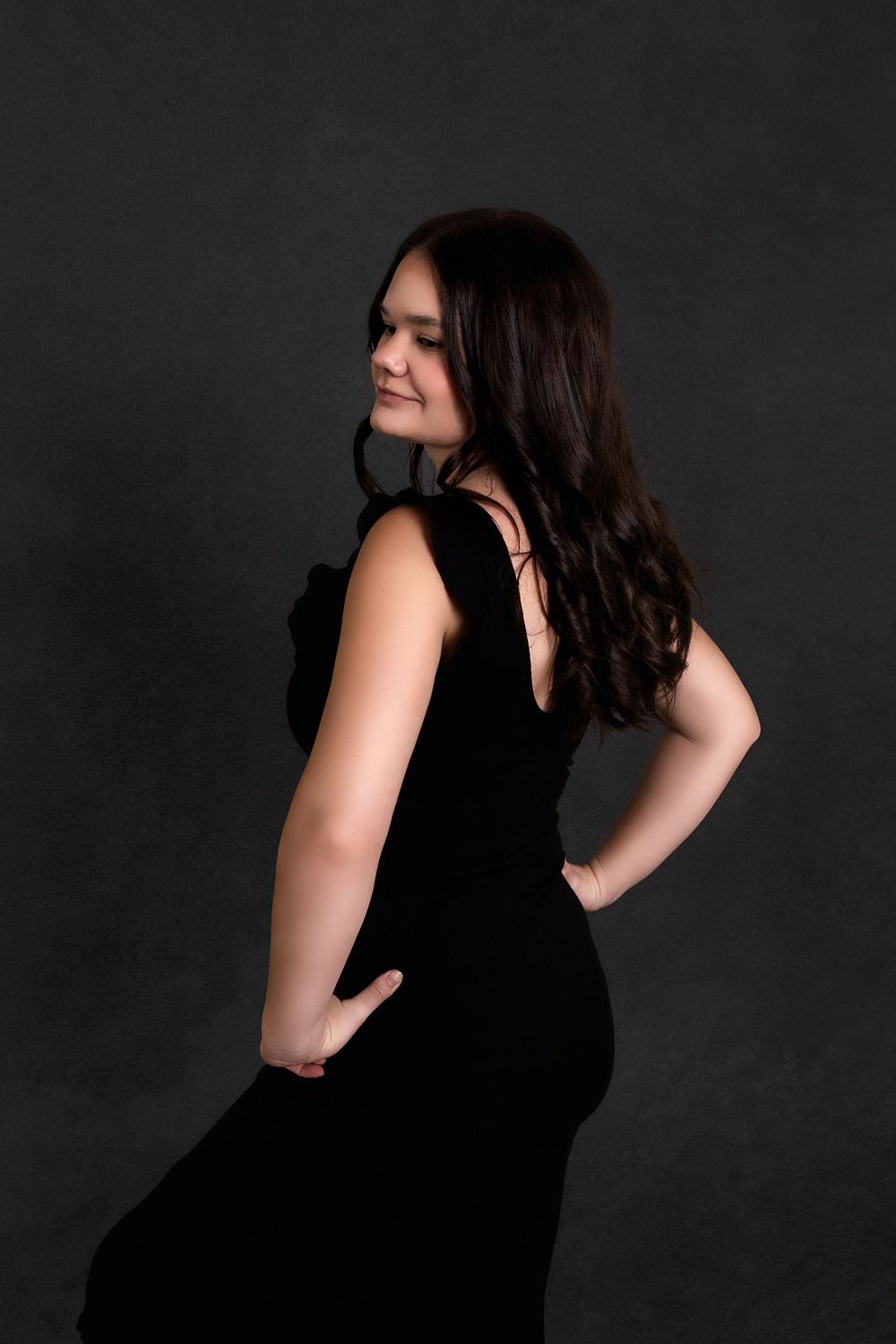 Woman in black dress poses against dark background in dramatic portrait series.