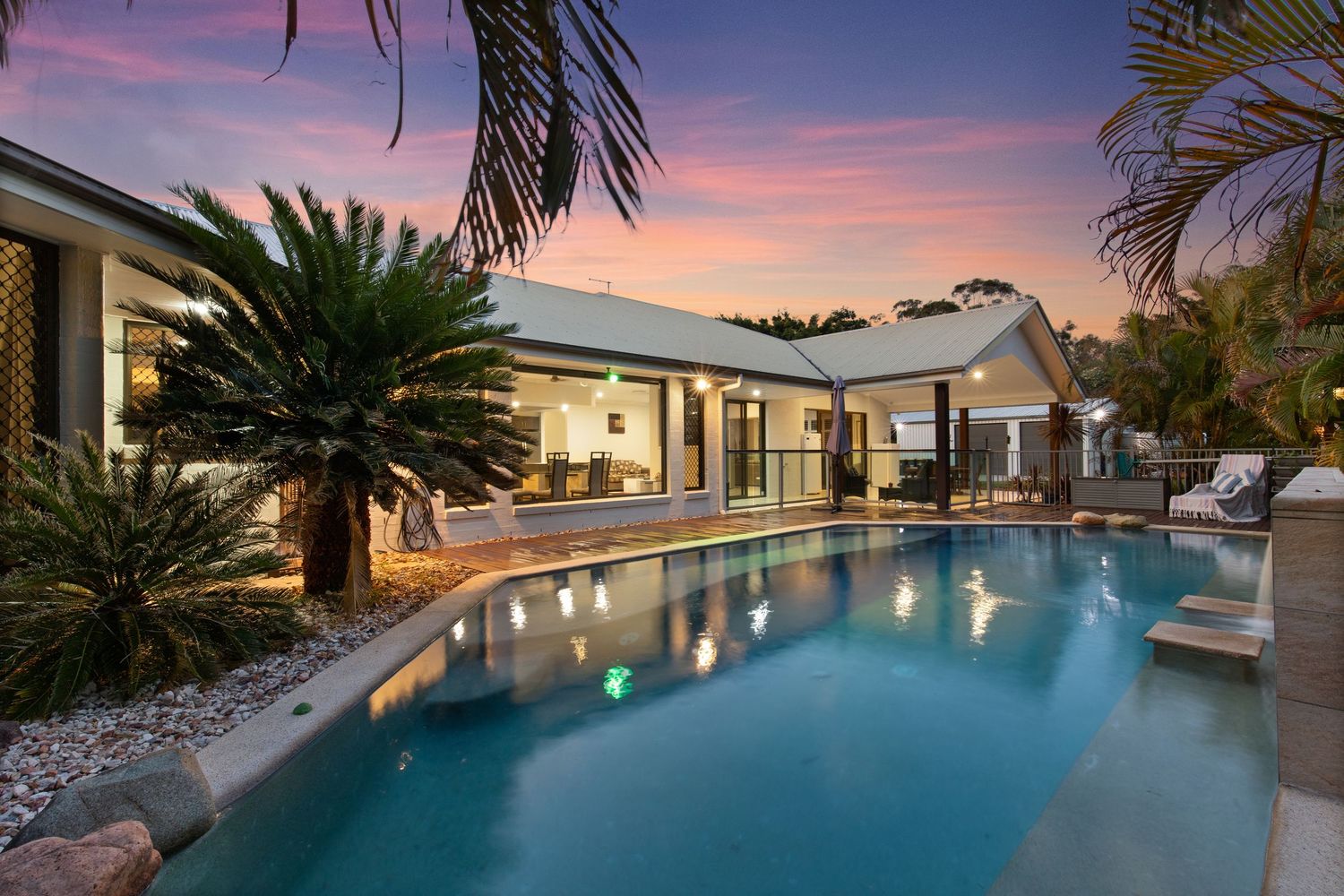Stunning resort-style pool with tropical landscaping and illuminated home at twilight sunset.