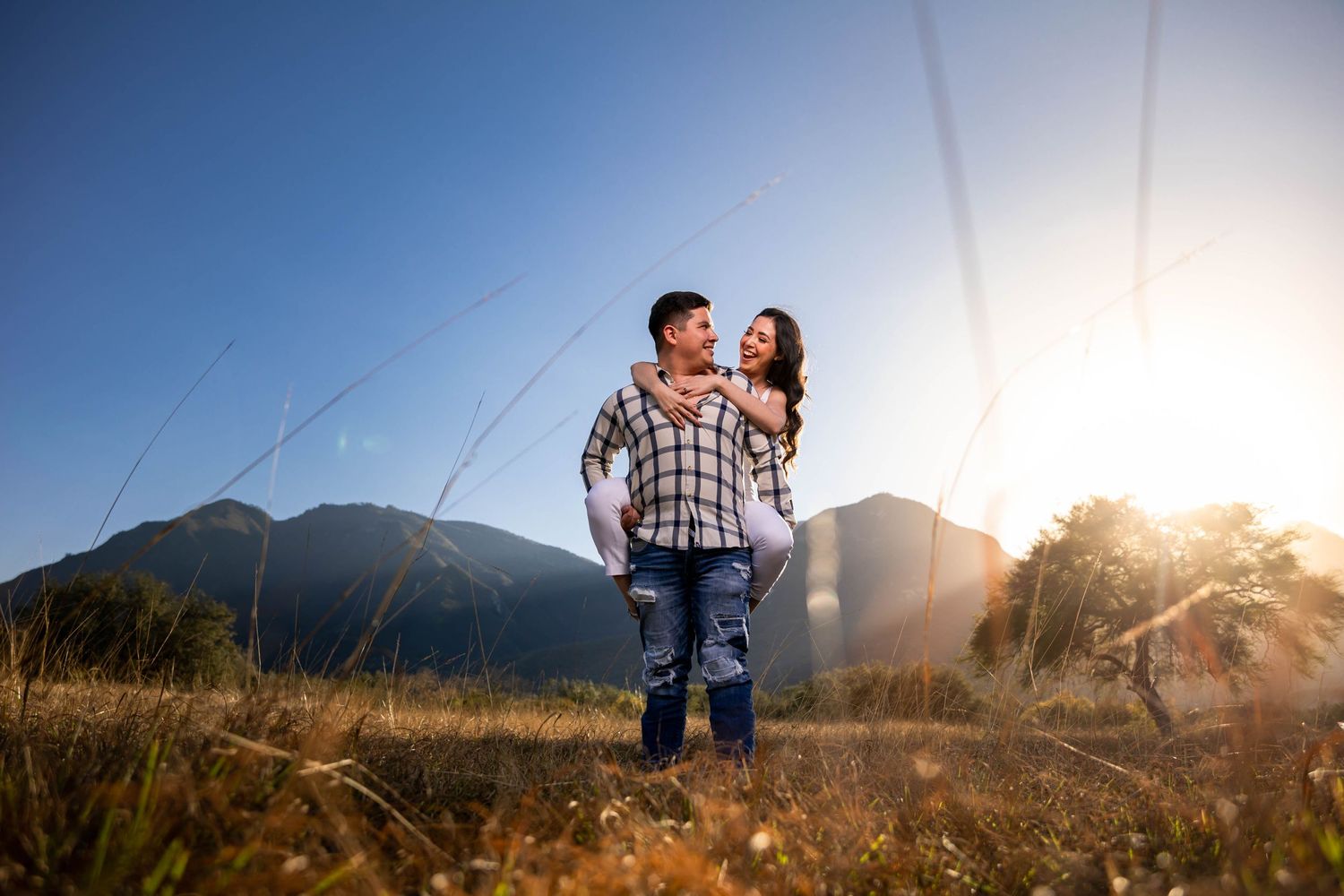 A romantic couple's portrait at sunset with mountains in the background.