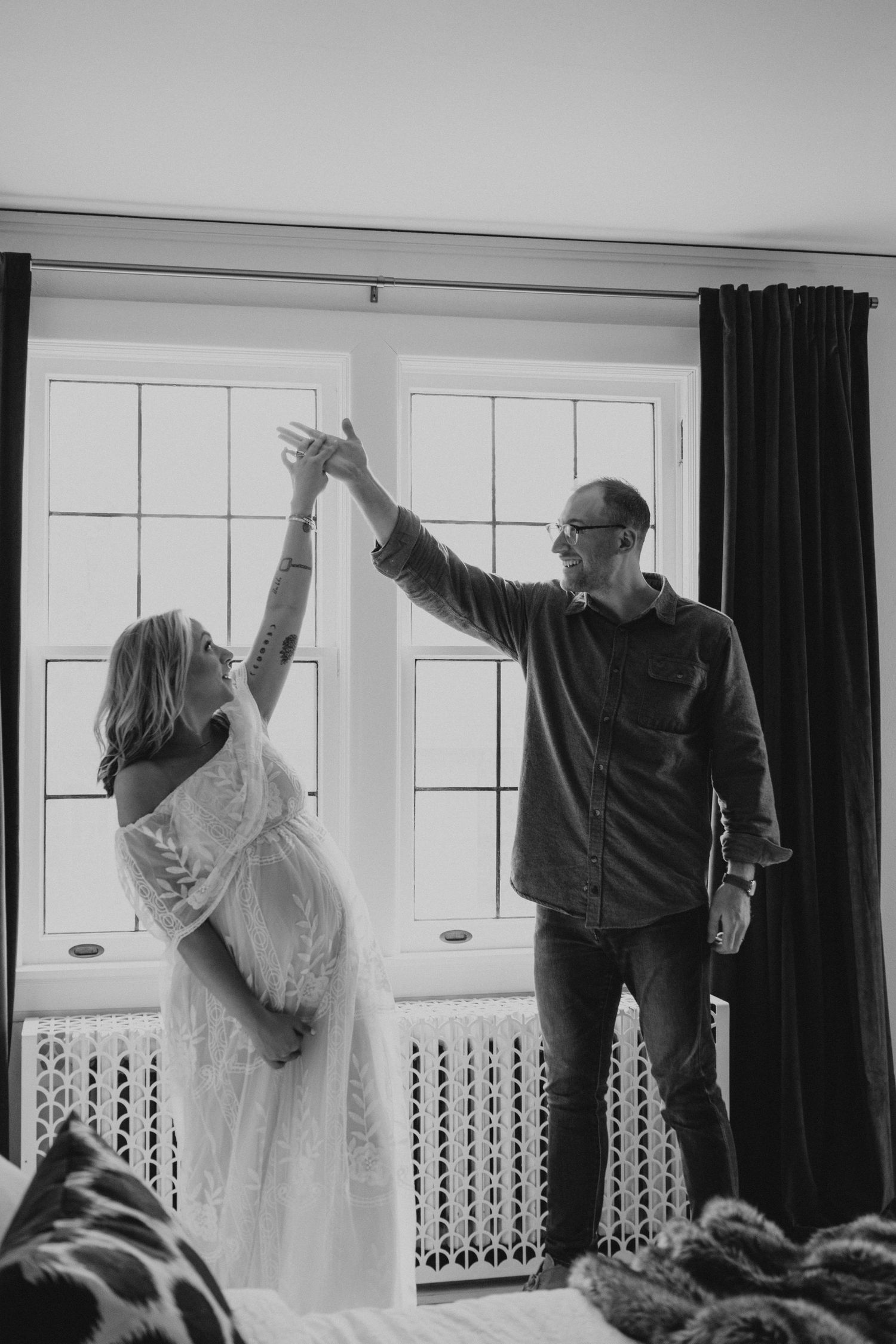 A couple dances together in a sunlit room with windows, while the woman wears a flowing white dress.