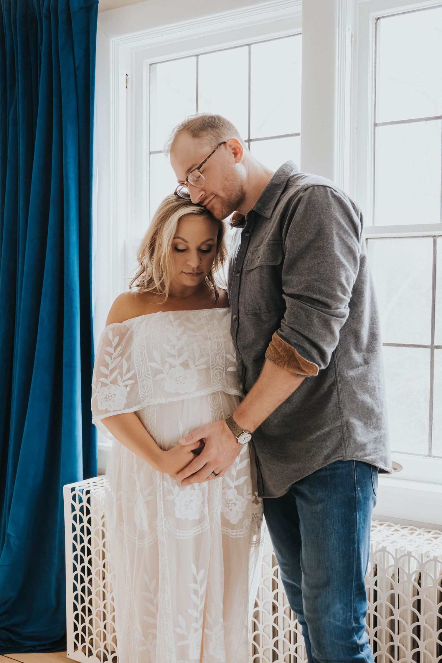 A tender moment captured between a couple near a window with blue curtains and white decor.