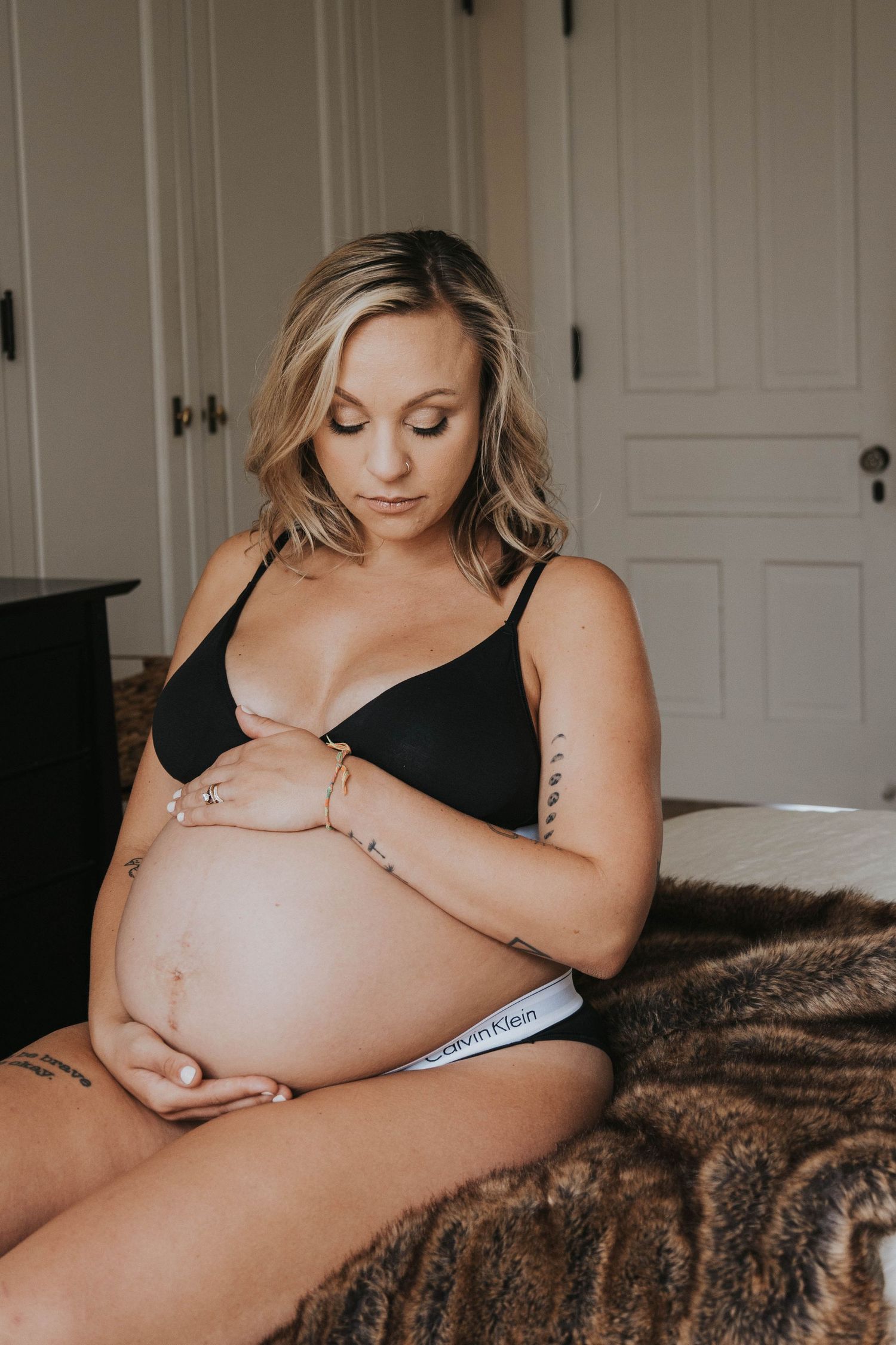 Intimate maternity photo capturing an expecting mother in black lingerie sitting on a brown fur blanket.