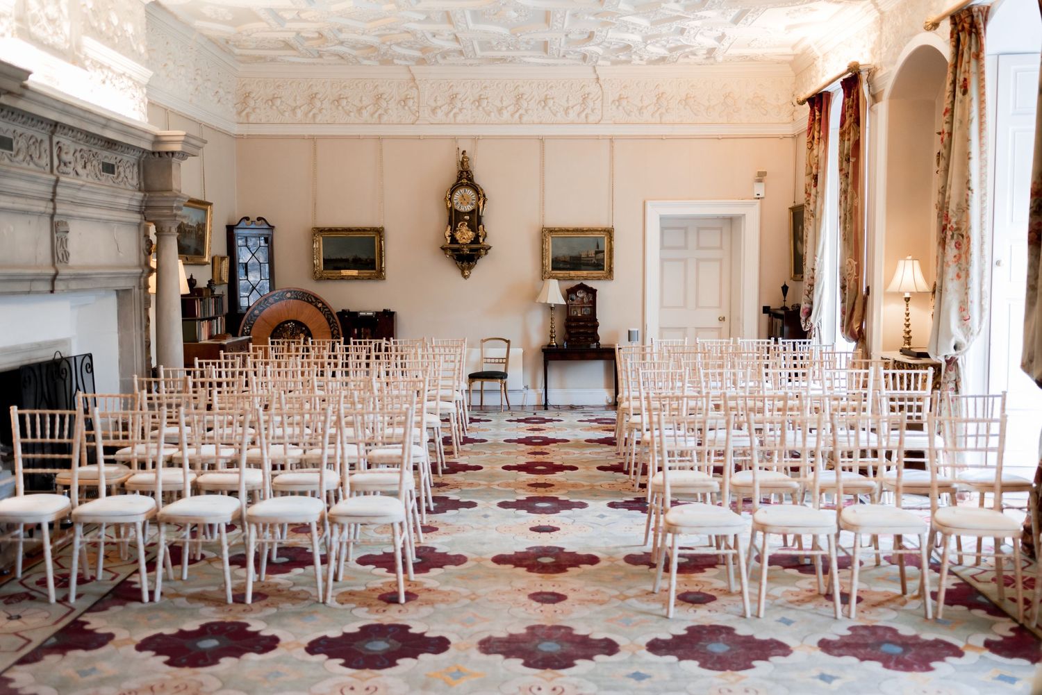 Elegant ornate ballroom with rows of white chairs on patterned marble floors and decorative crown molding details.