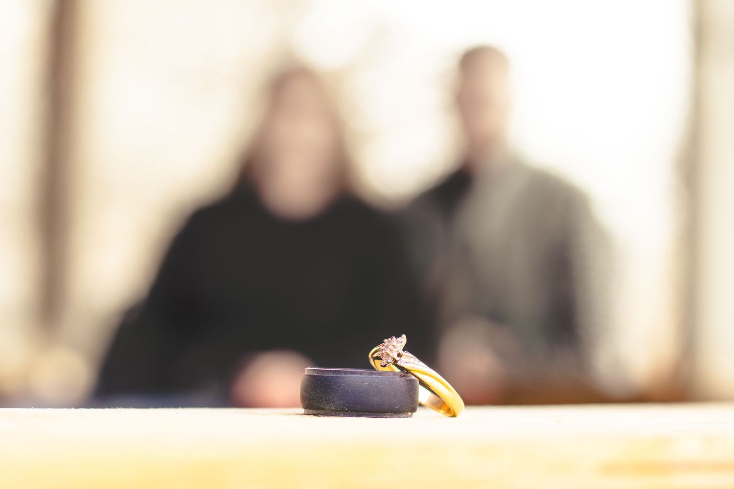 A couple sits on a park bench, showcasing their wedding rings while enjoying a moment together.