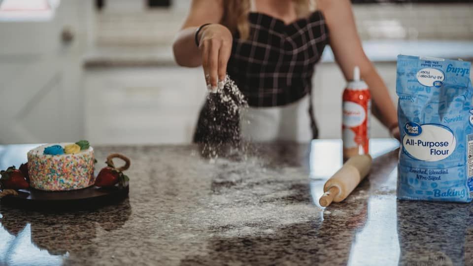 Hands sprinkling ingredients on a dark kitchen counter surface.